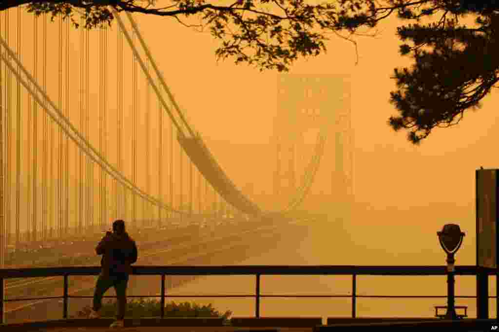 A Man talks on his phone as he looks through the haze at the George Washington Bridge from Fort Lee, New Jersey, June 7, 2023.