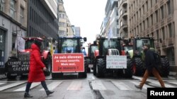 Orang-orang berjalan di depan traktor selama protes petani Eropa atas tekanan harga, pajak dan peraturan ramah lingkungan, pada hari pertemuan Menteri Pertanian Uni Eropa di Brussels, Belgia 26 Februari 2024. (REUTERS/Yves Herman)