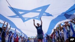 Manifestantes ondean una gran bandera israelí durante una protesta contra los planes del gobierno del primer ministro Benjamin Netanyahu para reformar el sistema judicial, frente a la Knesset, el parlamento de Israel, en Jerusalén, el lunes 24 de julio de 2023.