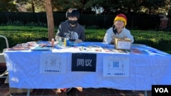 纪念白纸运动一周年的中国留学生和异议人士在南加州大学主校区大门口设有展位，桌上摆放着有关白纸运动的传单、签字笔、固体胶、艺术画布、明信片、“抗争贴画”等。 （美国之音/张木林）
