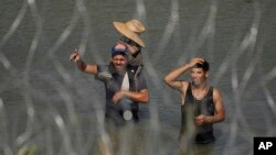 Migrants stand in the Rio Grande try to enter the U.S. from Mexico near the site where workers are assembling large buoys to be used as a border barrier in Eagle Pass, Texas.
