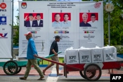 Officials carry ballot boxes past election candidate posters after being transported by motorboat to the Seribu Islands in Jakarta, February 9, 2024, ahead of Indonesia's presidential and legislative elections scheduled to be held on February 14.  (BAY ISMOYO / AFP)
