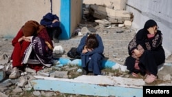 People rest next to damaged buildings as Palestinian arrive in Rafah after being evacuated from Nasser Hospital in Khan Younis due to the Israeli ground offensive against Hamas, in the southern Gaza Strip, Feb. 15, 2024.