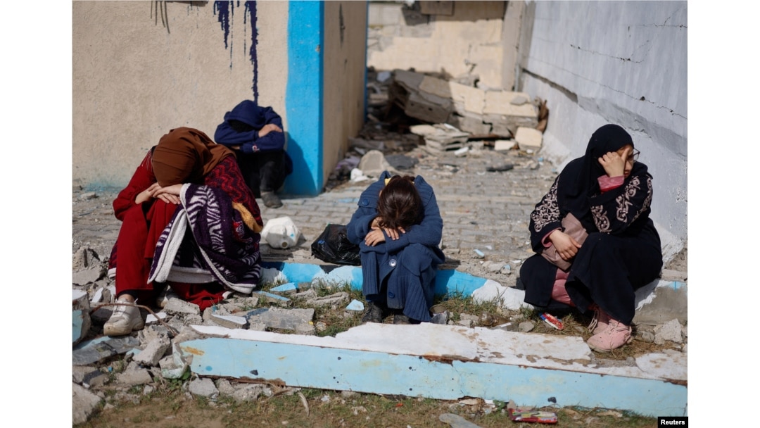 People rest next to damaged buildings as Palestinians arrive in Rafah, having been evacuated from Nasser Hospital in Khan Younis because of the Israeli ground offensive against Hamas, in the southern Gaza Strip, Feb. 15, 2024.
