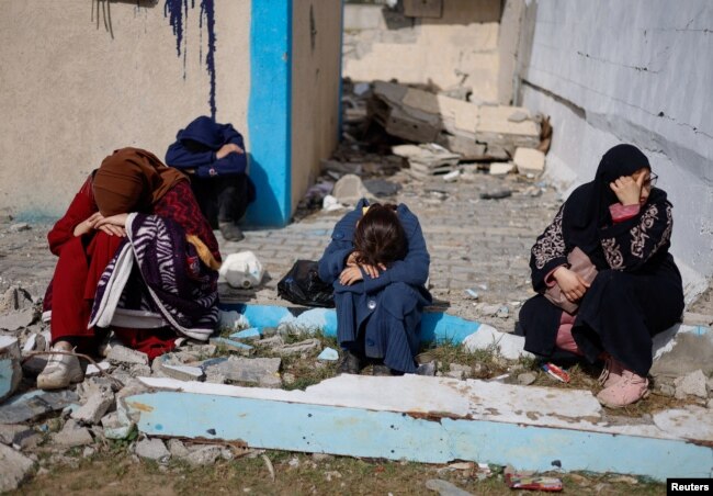 People rest next to damaged buildings as Palestinians arrive in Rafah, having been evacuated from Nasser Hospital in Khan Younis because of the Israeli ground offensive against Hamas, in the southern Gaza Strip, Feb. 15, 2024.