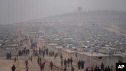 Warga Suriah berjalan melintas di depan kamp pengungsi yang dikelola oleh Bulan Sabit Merah Turki di distrik Sarmada, Idlib, Suriah, 26 November 2021. (Foto: Francisco Seco/AP Photo)