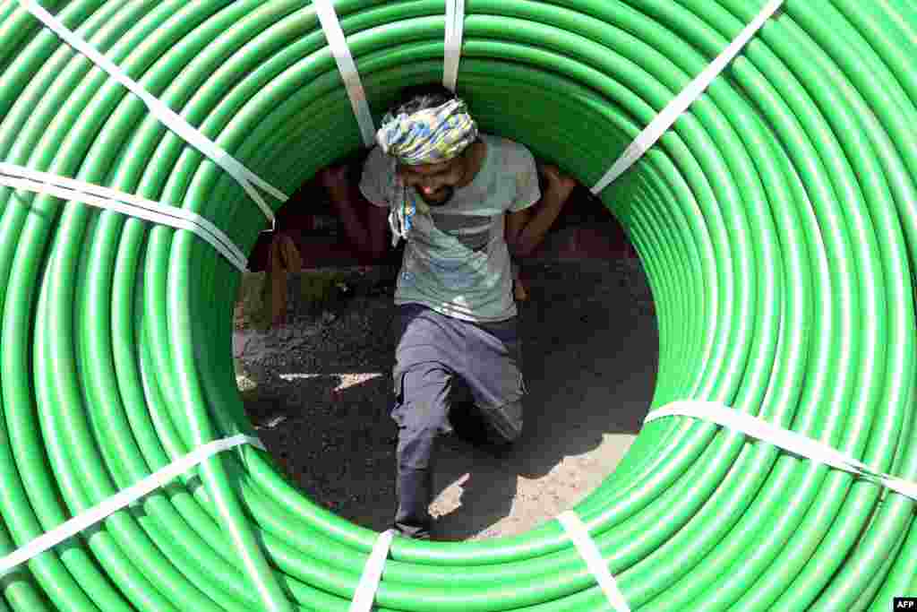 A laborer carries plastic pipe rolls at a railway store in Jalandhar, India. (Photo by Shammi Mehra / AFP)