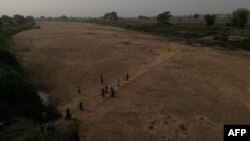 FILE - This aerial view shows refugee women crossing the dry beds of the White Volta river to their farms in Burkina Faso from Issakateng-Bausi, in Bawku, northern Ghana, on December 7, 2022.