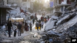 Palestinians displaced by the Israeli air and ground offensive on the Gaza Strip walk through a dark streak of sewage flowing into the streets of the southern town of Khan Younis, Gaza Strip, July 4, 2024.