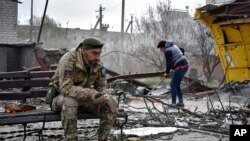 A Ukrainian serviceman smokes as a local resident clears debris near a building damaged in the Russian air raid in the town of Orikhiv, Zaporizhzhia region, Ukraine, April 5, 2024.