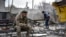 A Ukrainian serviceman smokes as a local resident clears debris near a building damaged in the Russian air raid in the town of Orikhiv, Zaporizhzhia region, Ukraine, April 5, 2024.