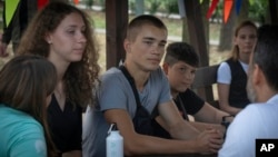 Valerii Soldatenko, 16, from Luhansk region under Russian occupation, center, and Kseniia Kucher, 16, from Kharkiv, left, talk with teachers in the rehabilitation camp for children affected by war, Aug. 27, 2024, in Uzhhorod, Ukraine.