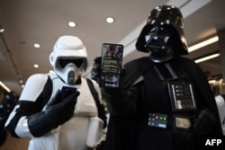 ILUSTRASI - Seorang cosplayer berpakaian karakter Star Wars Darth Vader (kanan) memegang ponsel yang menampilkan peringatan Pemerintah di Konvensi Fiksi Ilmiah Scarborough di Scarborough, 23 April 2023. (OLI SCARFF / AFP)