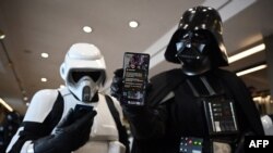A cosplayer dressed as the Star Wars character Darth Vader (R) holds a mobile phone displaying the Government alert issued to all smartphones to test life-threatening emergencies, at the Scarborough Sci-Fi Convention in Scarborough, north-east England, April 23, 2023.
