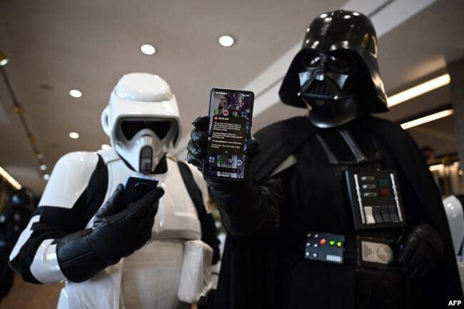 ILUSTRASI - Seorang cosplayer berpakaian karakter Star Wars Darth Vader (kanan) memegang ponsel yang menampilkan peringatan Pemerintah di Konvensi Fiksi Ilmiah Scarborough di Scarborough, 23 April 2023. (OLI SCARFF / AFP)