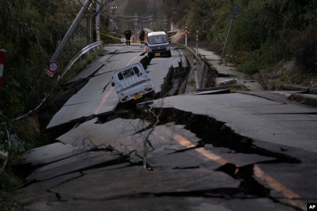 Bystanders look at damages somewhere near Noto town in the Noto peninsula facing the Sea of Japan, northwest of Tokyo, Tuesday, Jan. 2, 2024. (AP Photo/Hiro Komae)