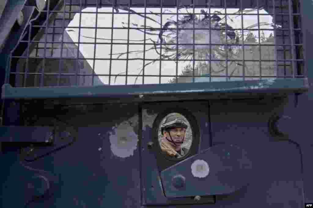 A member of a Kosovo police special unit is seen behind an armored vehicle's door damaged by bullets as he stands guard in an area around the Banjska Monastery in Banjska, north Kosovo, some 15km from the border with Serbia.