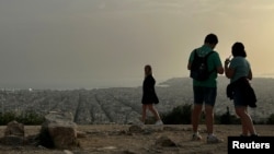 FILE - Tourists visit the Filopappou Hill, as Greece is hit by high temperatures and Saharan dust due to southern winds, in Athens, Greece, April 2, 2024.