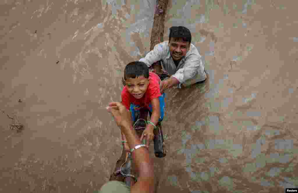 A man helps his son to climb onto a flyover under construction, after being displaced by the rising water level of river Yamuna after heavy monsoon rains in New Delhi, India, July 12, 2023.