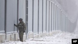 FILE - A Polish border guard stands next to the border wall in Nomiki in November 2022. Poland’s governing party is being rocked by reports that Polish consulates issued visas in Africa and Asia in exchange for bribes, opening the door for migrants to enter the EU.