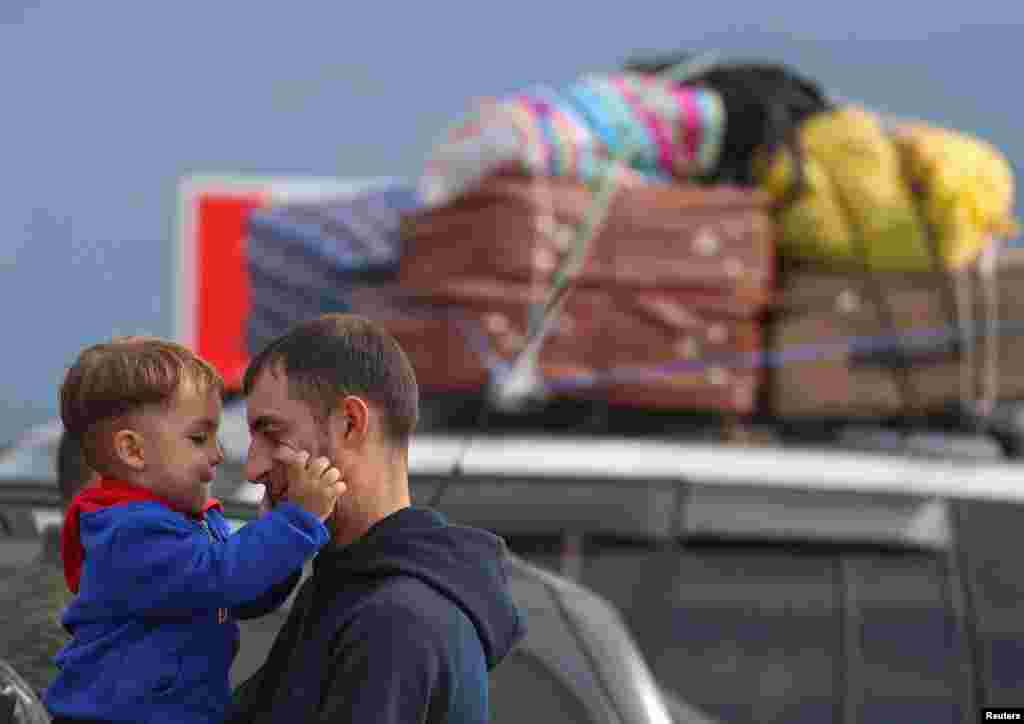 A refugee from Nagorno-Karabakh region holds a child while standing next to a car upon their arrival in the border village of Kornidzor, Armenia.