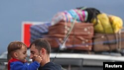 A refugee from Nagorno-Karabakh region holds a child while standing next to a car upon their arrival in the border village of Kornidzor, Armenia.