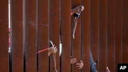 FILE - Migrants waiting to apply for asylum between two border walls hold out phones in hopes of getting a charge on May 11, 2023, in San Diego. 