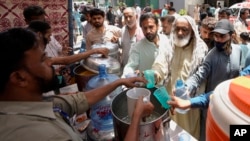 FILE - Volunteers provide lime sugar water to people at a camp set up to prevent heat stroke on a hot day in Karachi, Pakistan, May 23, 2024.