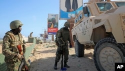 FILE - Ugandan peacekeepers with the African Union Transition Mission in Somalia (ATMIS) stand next to their armored vehicle on a street in Mogadishu, Somalia, May 10, 2022.