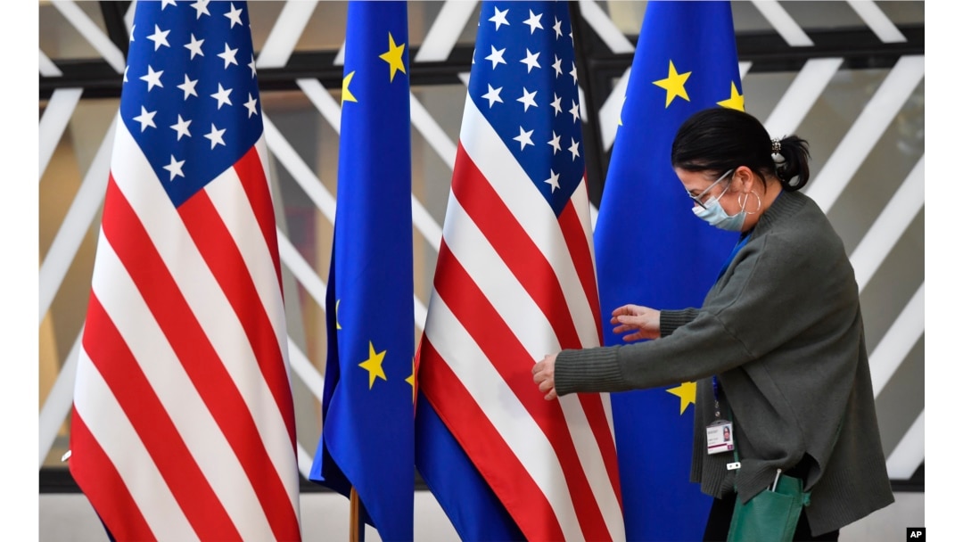 Anggota protokol sedang membenahi letak bendera Amerika Serikat dan Uni Eropa sebelum pertemuan luar biasa menteri luar negeri Uni Eropa di Brussels, 4 Maret 2022. (Foto: AP)