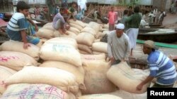 বাংলাদেশের একটি বাজারের পাশে নৌকায় ধানের বস্তা বোঝাই করছে কৃষকরা। (ফাইল ছবি) 