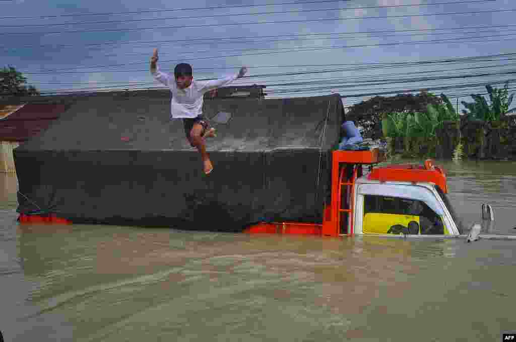 A boy jumps into the floodwaters on the national highway caused by heavy rain and the river bursting in Demak, Central Java, Indonesia.