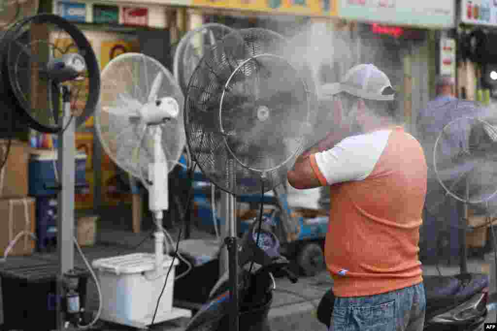 A man cools off with a mist dispenser set up on al-Jumhuriya street in central Baghdad, Iraq, amid soaring temperatures.