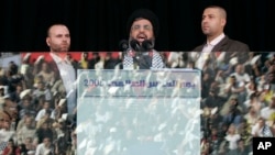 FILE - Hezbollah leader Sayyed Hassan Nasrallah, center, escorted by his bodyguard Yasser Nimr Qarnabsh, right, addresses supporters reflected in bulletproof glass in the southern suburbs of Beirut, Lebanon, Oct. 28, 2005. 