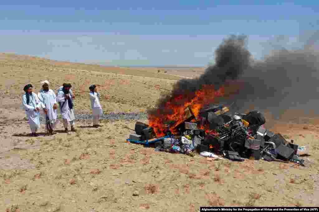 Members of Taliban stand guard after setting fire to a pile of musical instruments and equipment on the outskirts of Herat, July 29, 2023. 