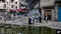Palestinians displaced by the Israeli air and ground offensive on the Gaza Strip walk next a dark streak of sewage flowing into the streets of the southern town of Khan Younis, Gaza Strip, July 4, 2024. 
