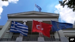 FILE - From left, Greek Turkish and European Union flags flutter in front of the Greek Foreign Ministry building ahead of a meeting of Greek and Turkish officials, in Athens, May 31, 2021. Delegations from both countries met Monday at the Defense Ministry in Athens.