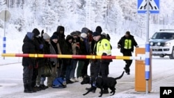 Migrants look at a Finnish Customs official's dog at the international border crossing at Salla, northern Finland, Nov. 22, 2023.