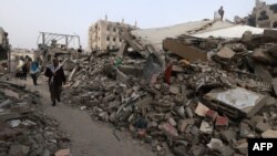 Orang-orang berjalan di dekat gedung-gedung yang hancur akibat pemboman Israel di Rafah di Jalur Gaza selatan, Minggu 25 Februari 2024.