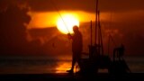 A fisherman reels in his catch as the sun rises over the Atlantic Ocean, June 28, 2023, in Bal Harbour, Florida.