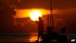 (FILE) A fisherman reels in his catch as the sun rises over the Atlantic Ocean.