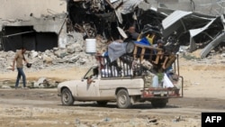 A Palestinian man drives a loaded pickup truck past destruction from previous Israeli bombardment in Khan Yunis in the southern Gaza Strip on June 21, 2024.