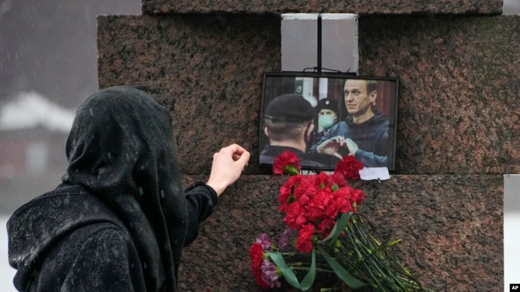 Bir kadın, 17 Şubat 2024'te Rusya'nın St. Petersburg kentindeki Siyasi Baskı Kurbanları Anıtı'na çiçek bıraktıktan sonra Alexey Navalny'nin fotoğrafına dokunuyor.