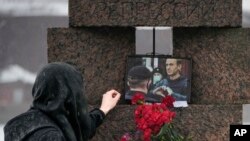 在俄罗斯圣彼得堡，一位女士在政治压迫受害者纪念碑敬献鲜花后触摸纳尔瓦尼的照片。(2024年2月17日)