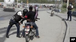 A police officer pats down a motorcyclist at a checkpoint in Port-au-Prince, Haiti, July 1, 2023. 