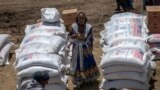 FILE - An Ethiopian woman stands by sacks of wheat to be distributed by the Relief Society of Tigray in the town of Agula, in the Tigray region of northern Ethiopia, May 8, 2021.
