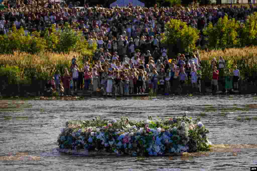 People standing on the banks of the Vistula river in Warsaw, Poland, look at a huge wreath floats on the water during the Wreaths over the Vistula festival, June 22, 2024.