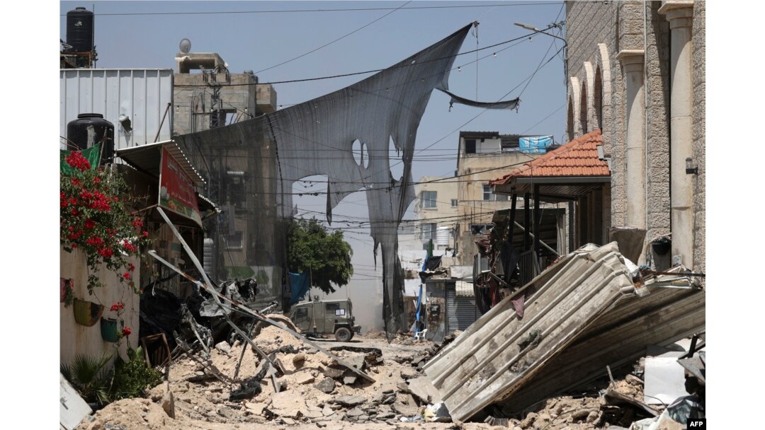 Sebuah kendaraan lapis baja terlihat di ujung jalan yang diblokir saat berlangsungnya operasi militer di kamp pengungsi Jenin di Tepi Barat yang diduduki Israel, 4 Juli 2023. (Jaafar ASHTIYEH/AFP)