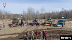 Funcionarios de defensa ucranianos posan frente a equipos militares suministrados desde el extranjero, incluido un tanque de batalla británico Challenger 2, en un lugar no identificado en Ucrania, el 27 de marzo de 2023.