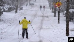 Nelson Taylor, of Providence, R.I., left, uses cross-country skis while making his way along a residential street, Feb. 13, 2024, in Providence.